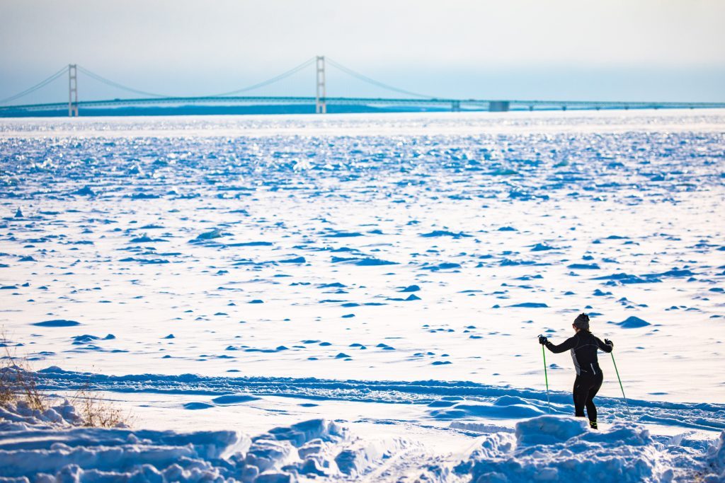 A cross-country skier cruises over the frozen water along Mackinac Island, with the Mackinac Bridge on the horizon