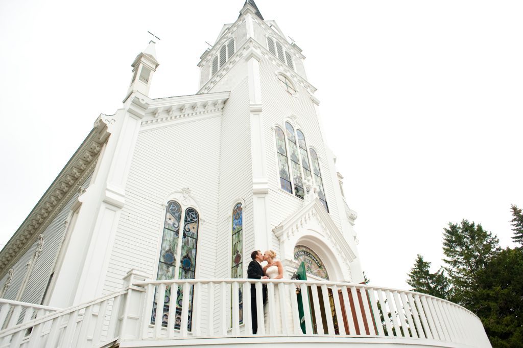 A bride and groom share a kiss outside Mackinac Island's historic Ste. Anne's Church wedding venue