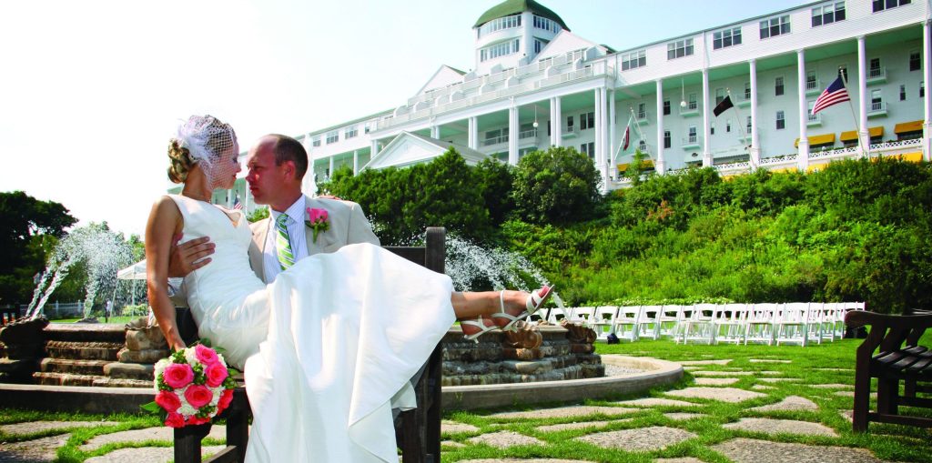 A newlywed groom holds his bride for a photo outside by the fountain at Mackinac Island's Grand Hotel