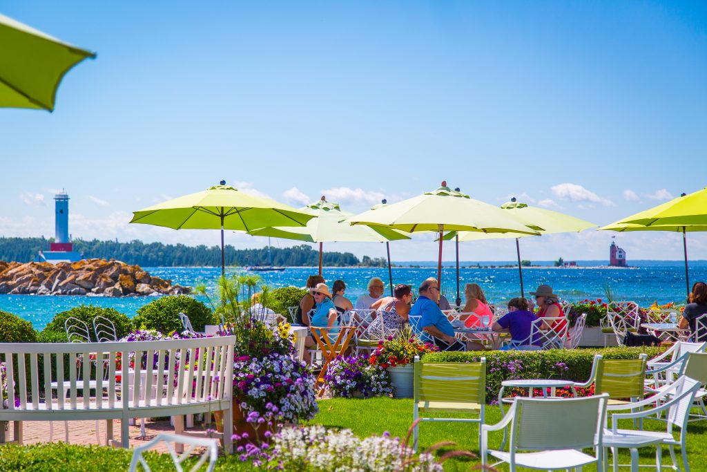 People dine under umbrellas out on the waterfront patio at Iroquois Hotel's Carriage House restaurant on a sunny day on Mackinac Island