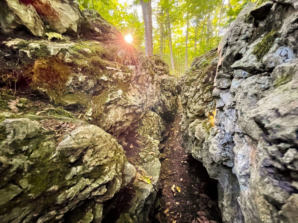 The sun shines over the top of Crack in the Island rock formation in the woods of Mackinac Island State Park
