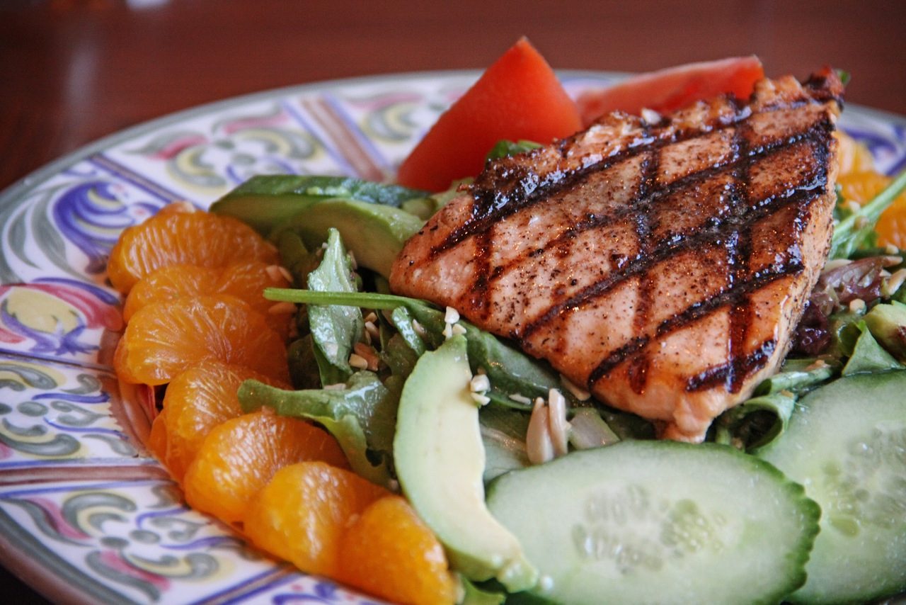 A plate of grilled fish on a bed of spinach with orange slices and cucumbers at a Mackinac Island restaurant