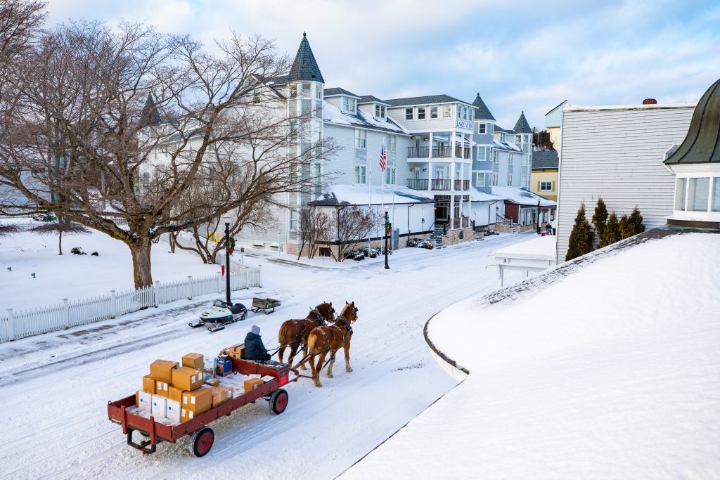 A horse-drawn dray loaded with boxes makes its way down a snowy Mackinac Island street in winter