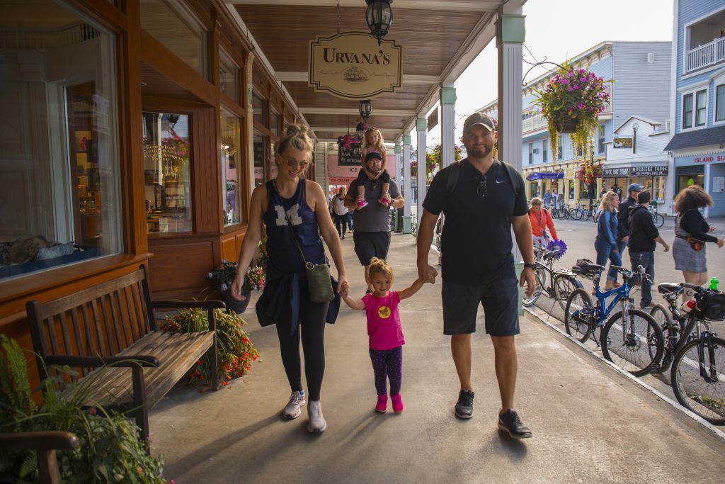 A young family walks past a row of shops and restaurants on Mackinac Island’s Main Street
