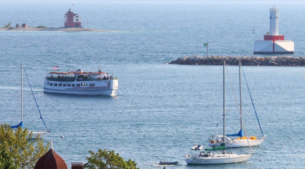 A Mackinac Island ferry boat enters the Mackinac Island harbor with Round Island Lighthouse in the background.