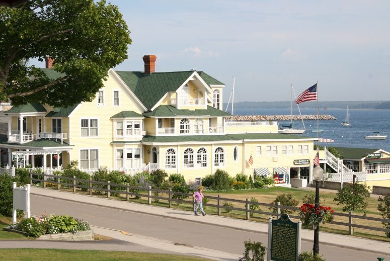 A person walks on the sidewalk past Mackinac Island's Bay View Inn on a beautiful sunny day by the water