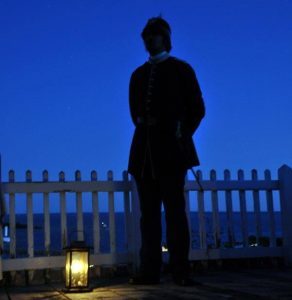 A soldier stands by a lantern and looks out from Mackinac Island's historic Fort Mackinac at night