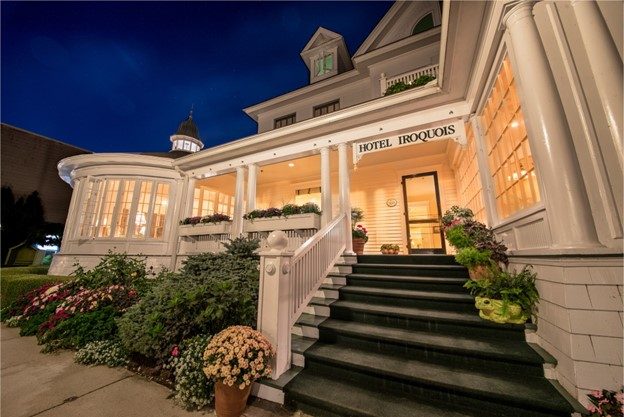 The front steps to Mackinac Island’s Hotel Iroquois at night with lights illuminating the porch and inside 