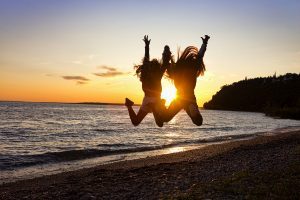 Two girls leap high into the air on a Mackinac Island beach, framing the setting sun for an epic photograph.