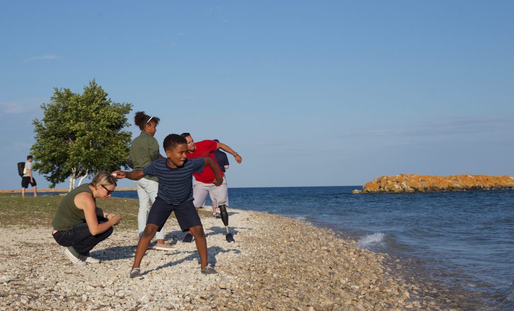 A family skips stones into the water from the beach at Mackinac Island’s Windermere Point.