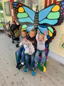 Four kids sit excitedly outside the Wings of Mackinac butterfly sign.