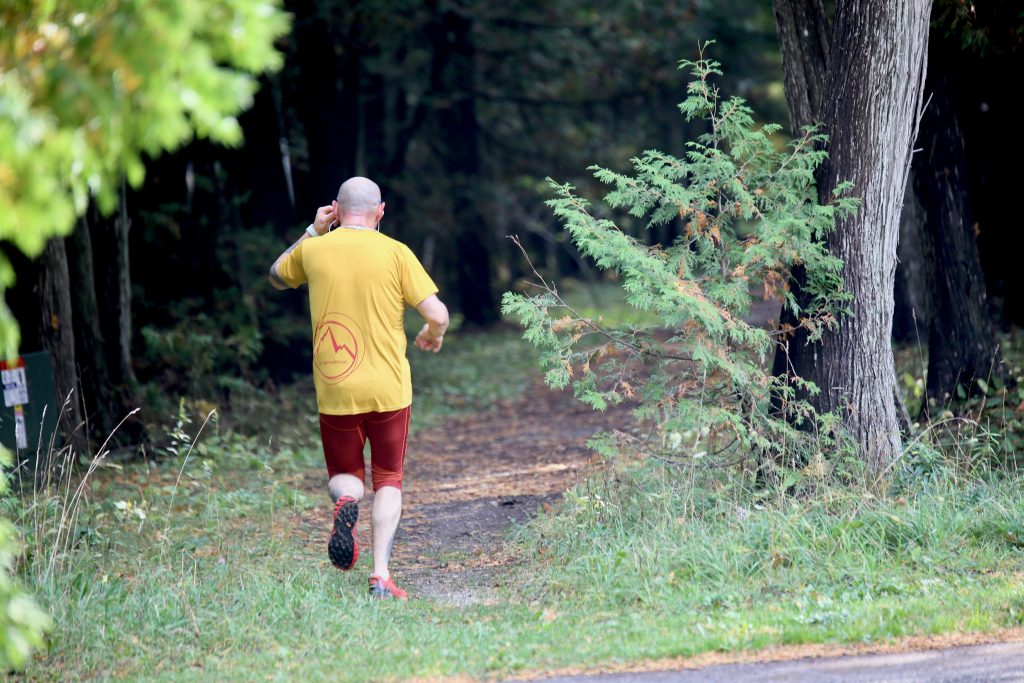 A man wearing ear buds runs down an earthen trail into the woods of Mackinac Island State Park