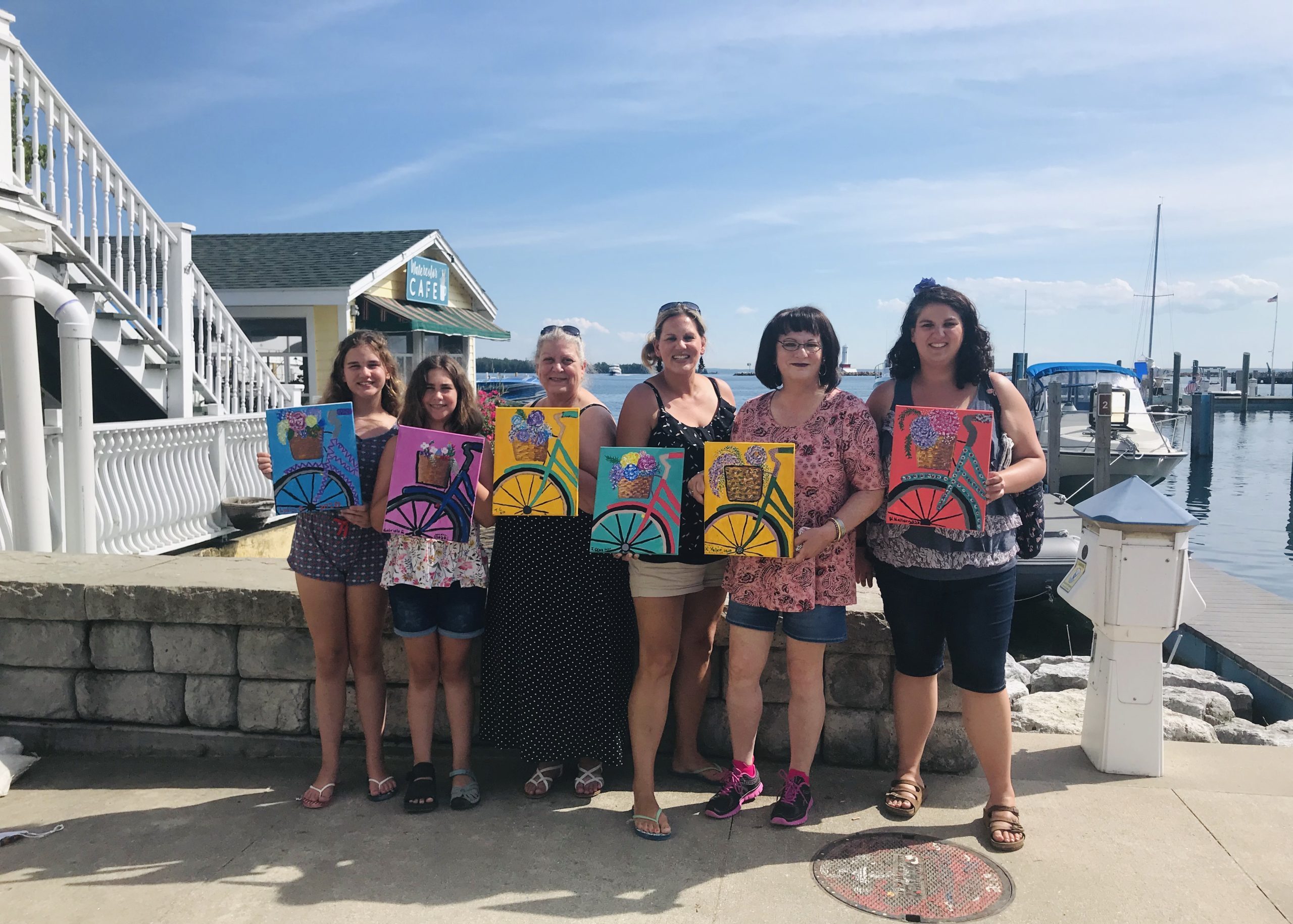 A group of women and girls show off the paintings they made in an art class at Watercolor Café on Mackinac Island