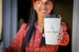 A barista at Lucky Bean on Mackinac Island hands a cup of coffee toward the camera.