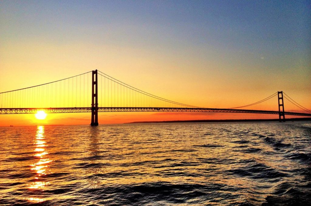 The sunset paints the water red, orange and yellow behind the Mackinac Bridge near Michigan’s Mackinac Island