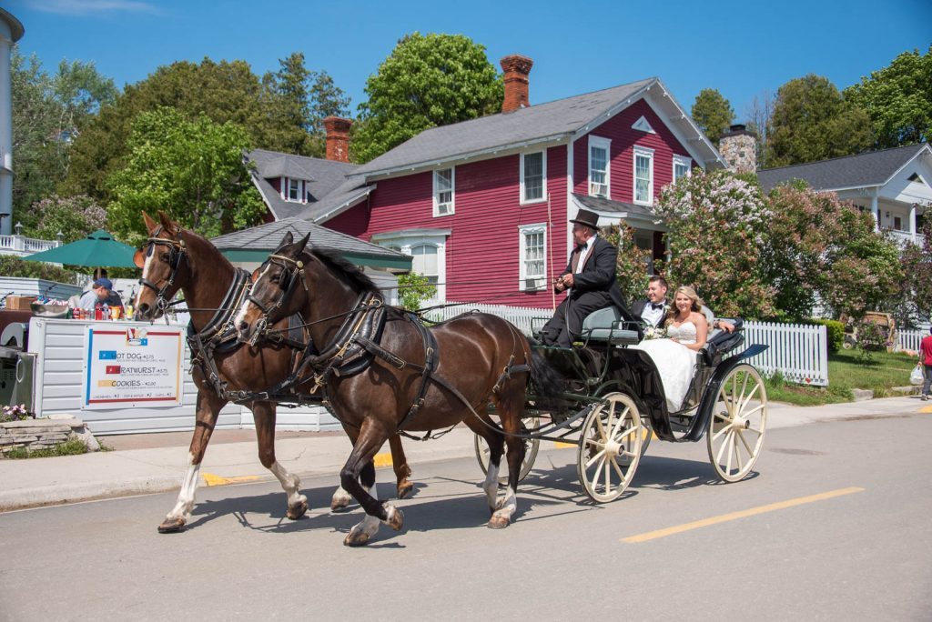A bride and groom enjoy a horse-drawn carriage ride through town after getting married on Mackinac Island
