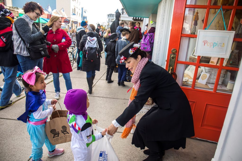 A shop owner bends down to put candy in the bags of young trick-or-treaters during Mackinac Island’s Halloween Weekend.