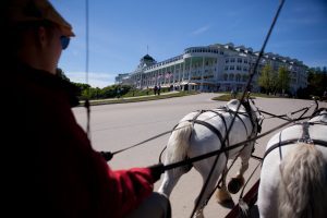 A horse-drawn carriage tour passes by historic Grand Hotel on the way to Mackinac Island State Park.