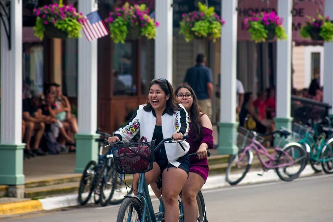 Two girls pedal a tandem bicycle down Mackinac Island's Main Street