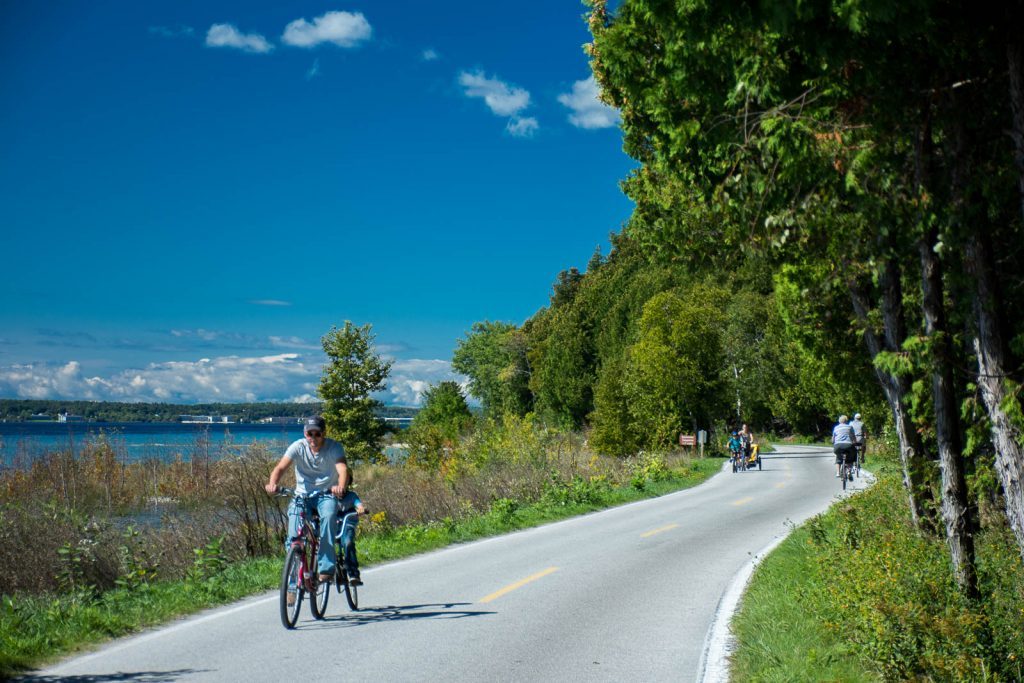 Mackinac Island visitors pedal bicycles including tandem bikes and burleys on picturesque M-185.