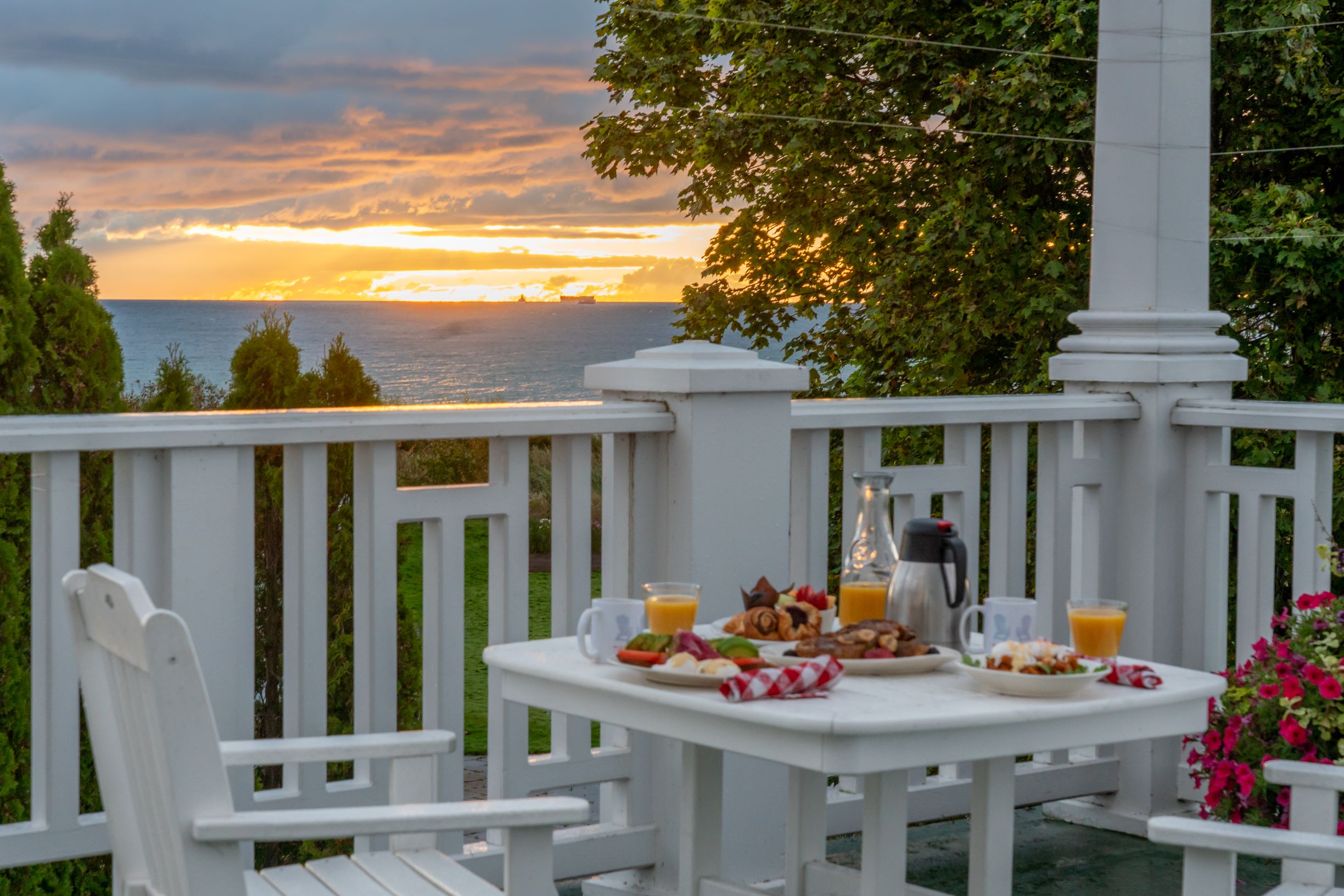 Plates of breakfast food cover a table in an outdoor dining area with a sunrise view of the water on Mackinac Island.