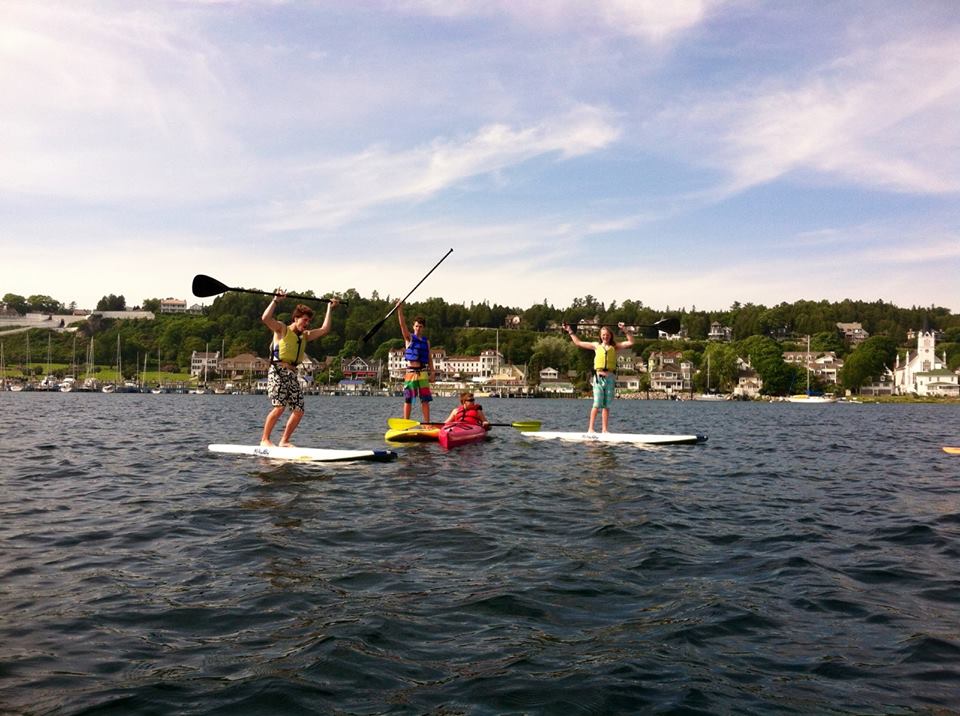 A group of teenagers take paddleboards and kayaks through the Mackinac Island harbor