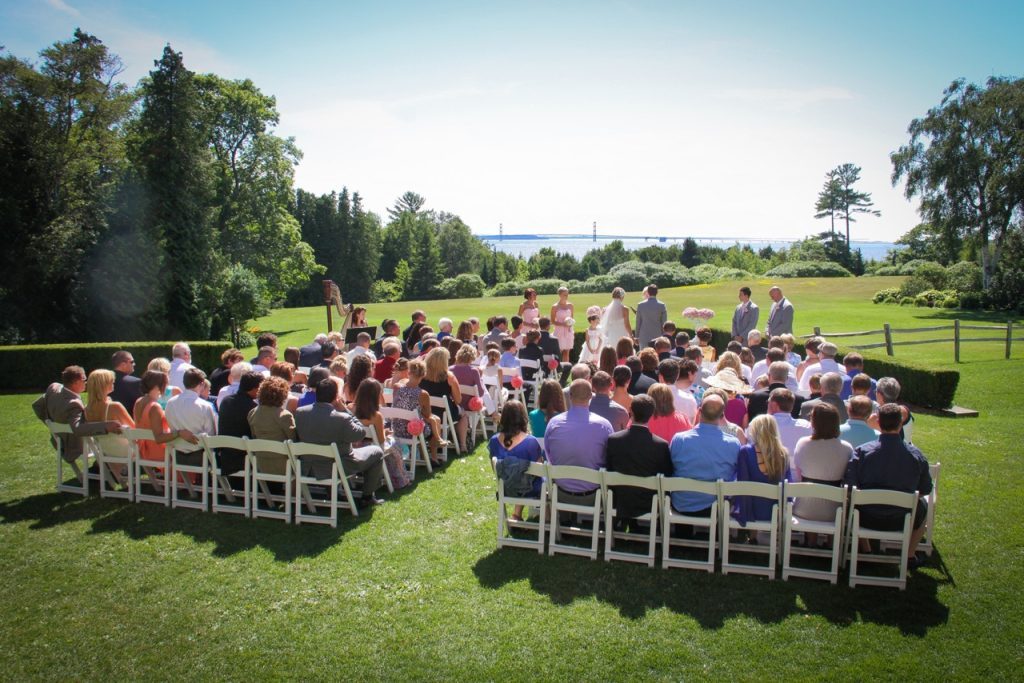 A wedding ceremony takes place in a beautiful setting overlooking the Mackinac Bridge on the lawn at Mackinac Island's Inn at Stonecliffe