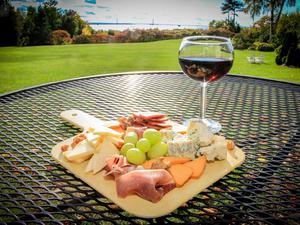A charcuterie board and glass of wine are set on an outdoor table overlooking the water on Mackinac Island