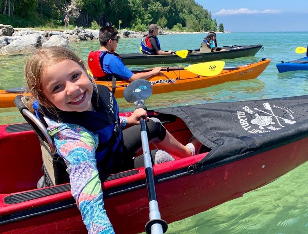 Young Girl Paddling in Kayak in Waters Around Mackinac Smiling at Camera