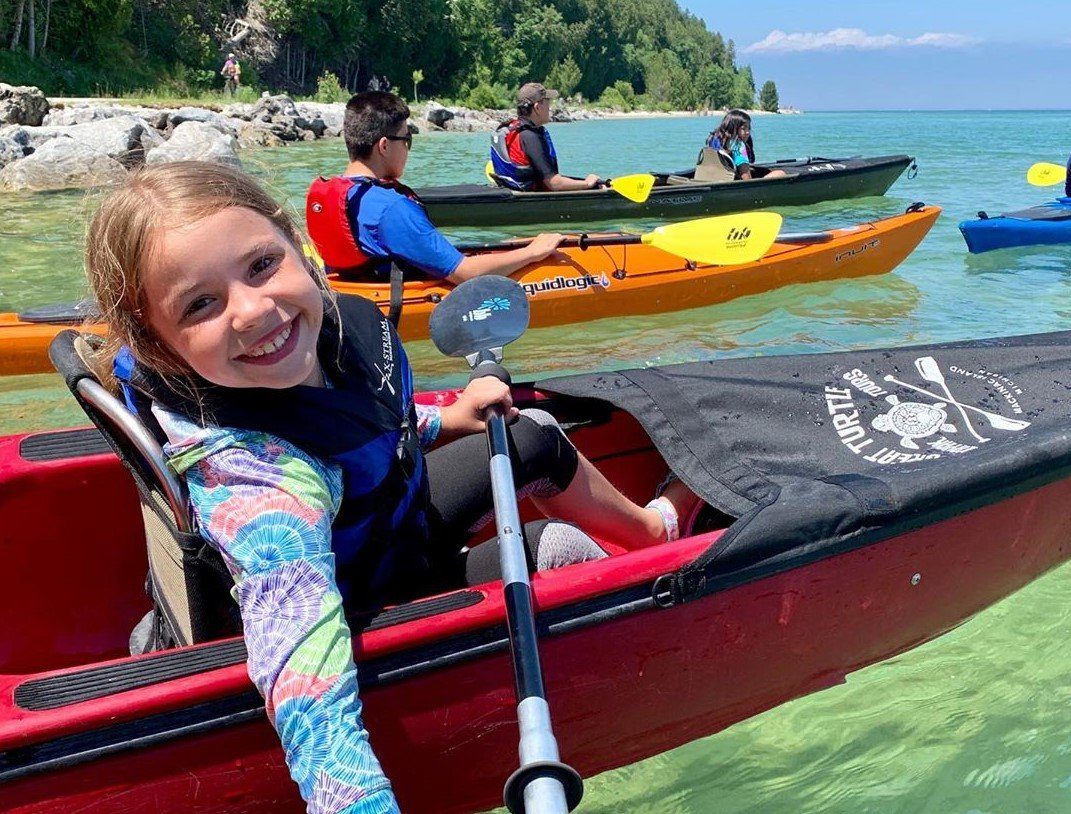 Young Girl Paddling in Kayak in Waters Around Mackinac Smiling at Camera