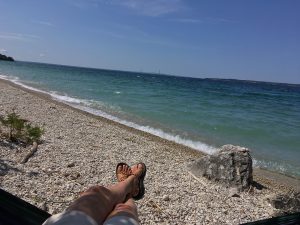 A person’s feet and hands stick out from a hammock on the rocky beach at Mackinac Island’s British Landing on Lake Huron