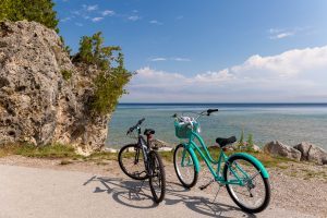 Two unoccupied bicycles stand parked on the side of a Mackinac Island road along the water
