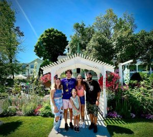 A family of five poses for a portrait in front of an archway in a colorful flower garden on Mackinac Island