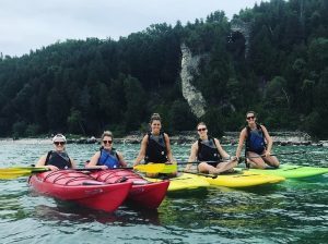 Five young women anchor side by side in kayaks with Mackinac Island's Arch Rock in the background
