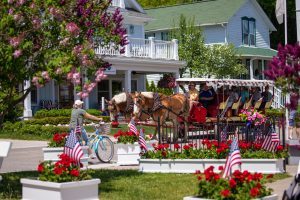 A horse-drawn taxi and a bicyclist pass a row of cottages on Mackinac Island