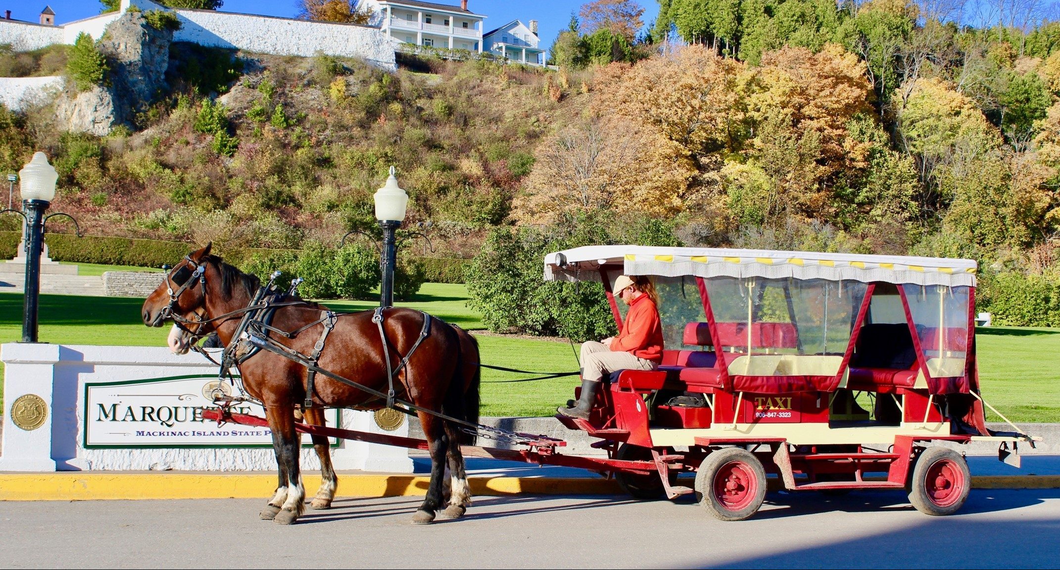 A horse-drawn taxi on Mackinac Island stops in front of Marquette Park at the foot of historic Fort Mackinac.