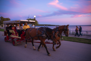 A horse-drawn taxi transports passengers along the Mackinac Island waterfront as the sun sets.