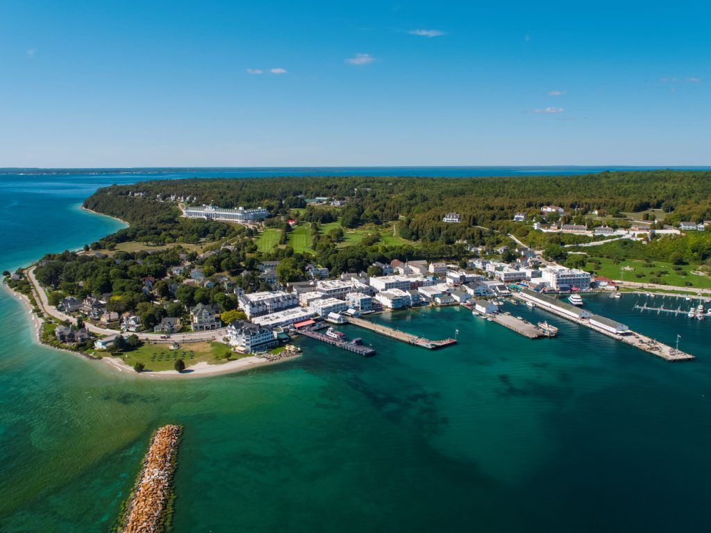 An aerial drone photograph of downtown Mackinac Island with Grand Hotel and golf course on the bluff