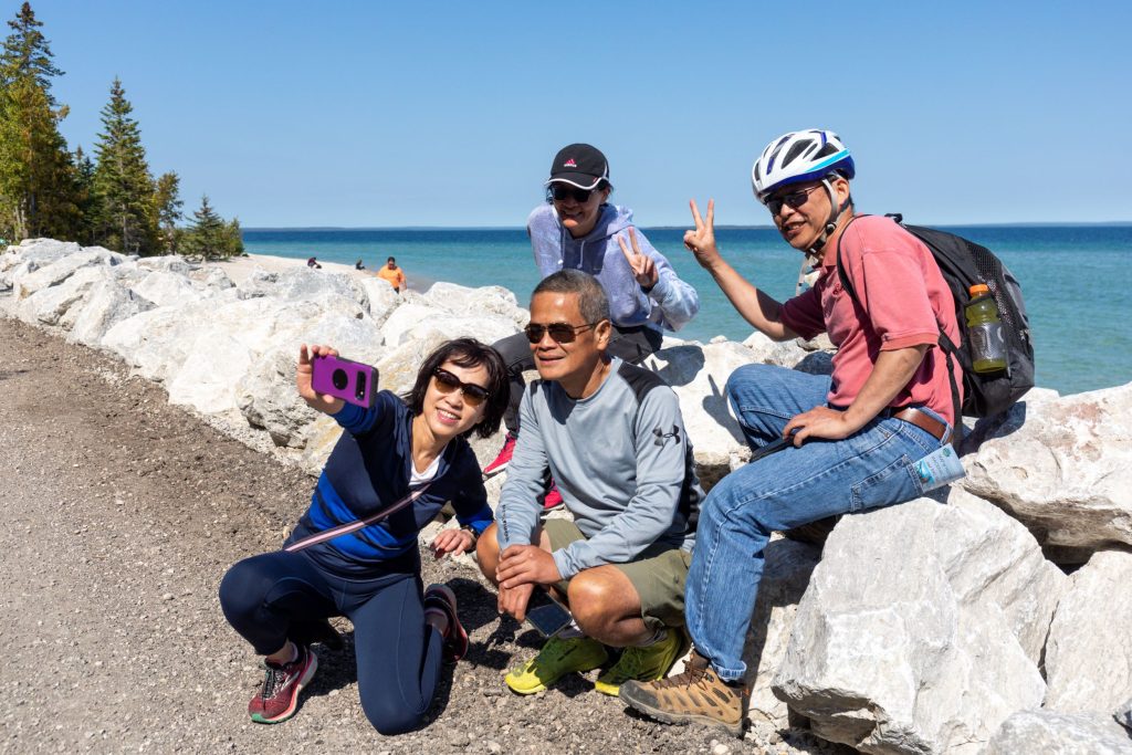 A family poses for a selfie along the rocks by the water on Mackinac Island