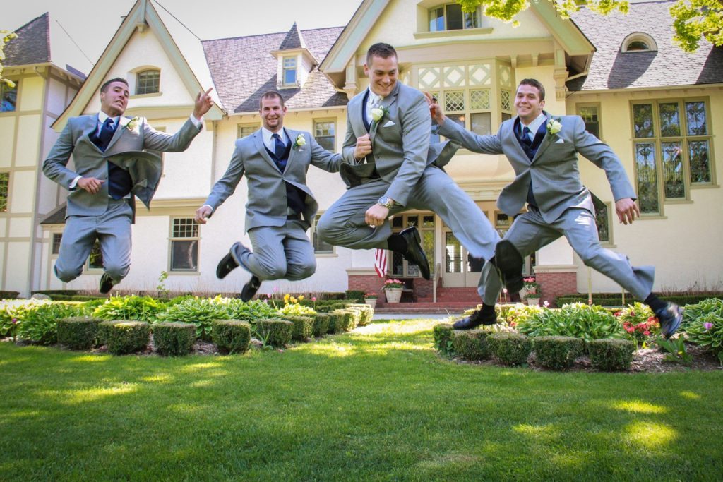 Four groomsmen jump on the lawn outside Mackinac Island's stately Inn at Stonecliffe