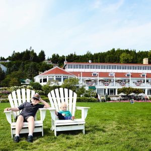 Two Brothers Sitting in White Adirondack Chairs Outside Historic Hotel on Mackinac Island