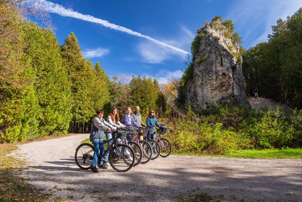 A family riding bikes on Mackinac Island poses for a photo in front of Sugar Loaf in Mackinac Island State Park