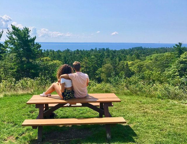 A young couple sits arm in arm on a picnic table looking out at the woods and water near Mackinac Island’s Fort Holmes