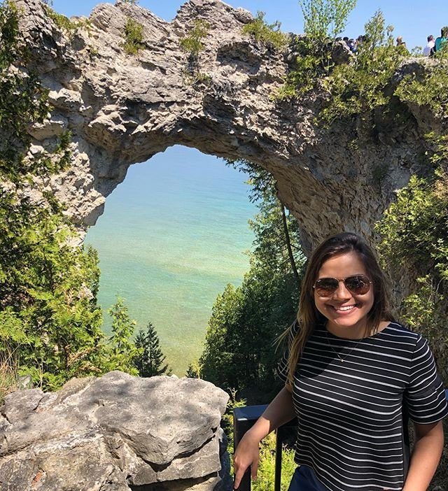 Young Woman With Sunglasses Smiling for Selfie Beside Arch Rock Over Waters Surrounding Mackinac Island