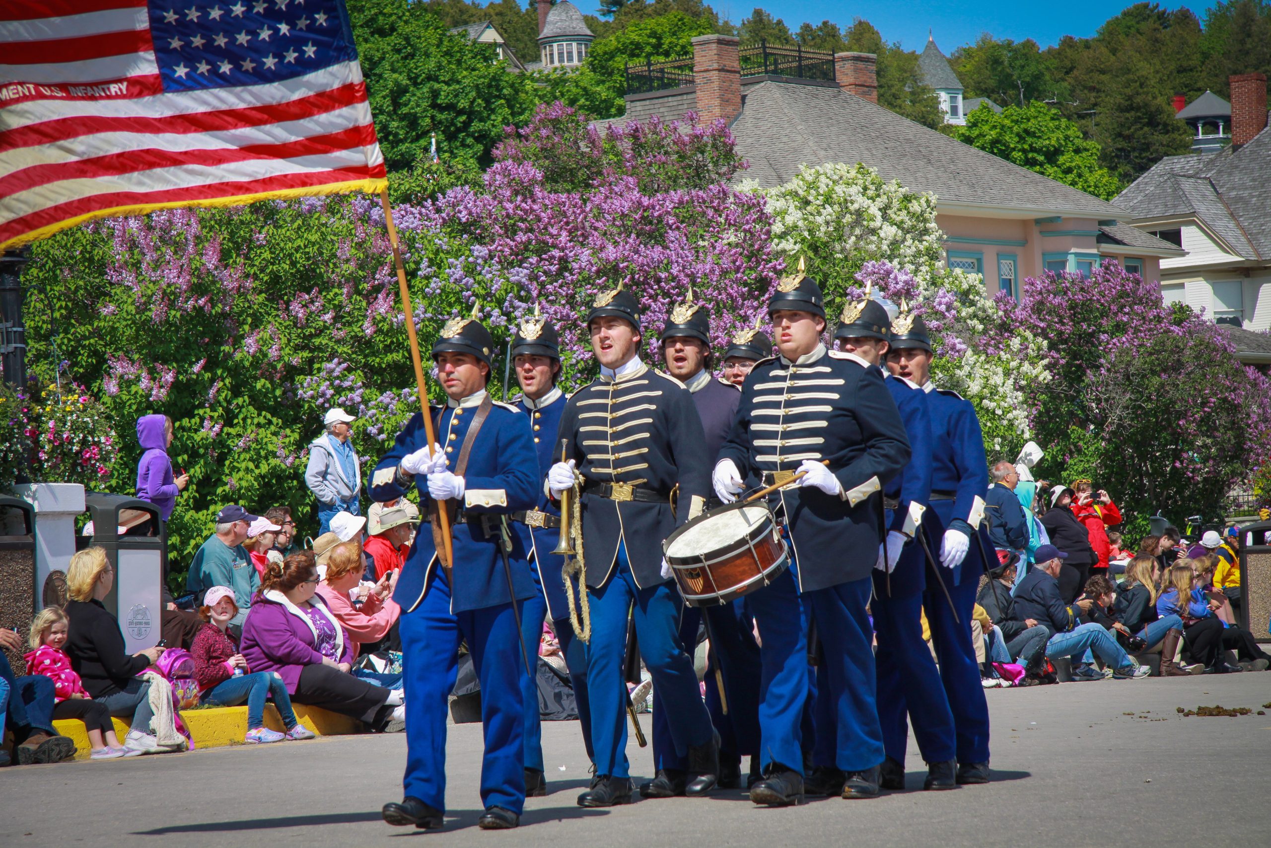 A group of interpretive soldiers walk down the street playing drums and carrying an American flag during a Mackinac Island parade