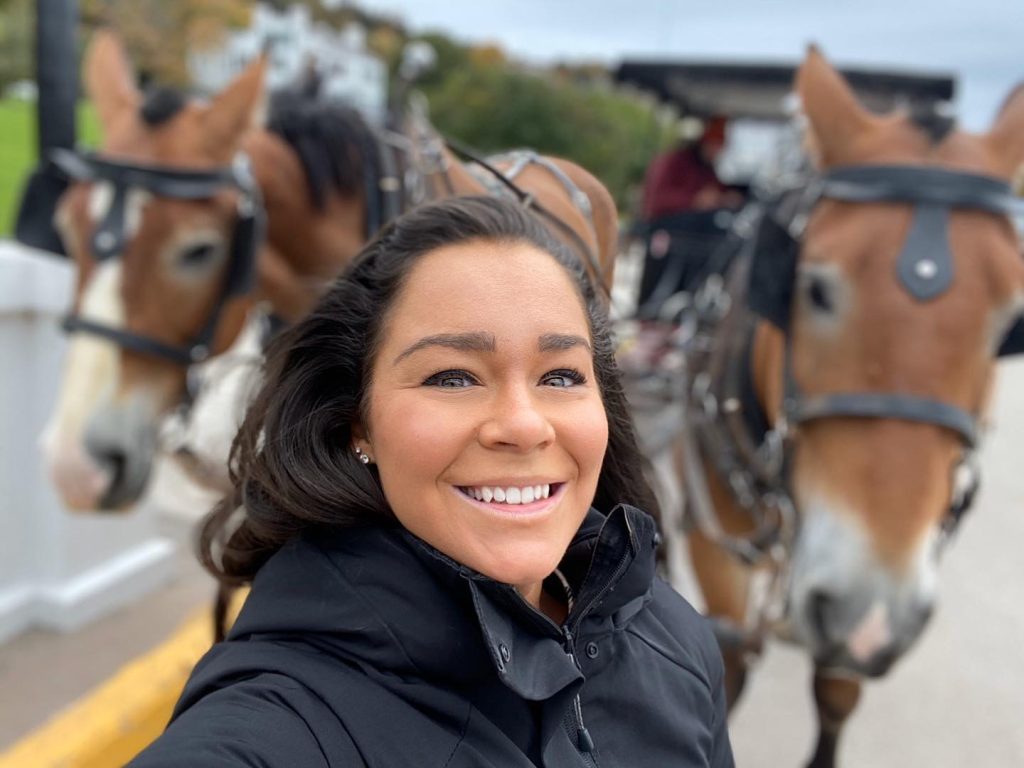 A woman snaps a selfie in front of two Mackinac Island horses