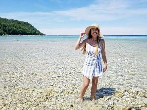 Woman in Sun Hat and Striped Dress Walking Barefoot in the water along a Mackinac Island beach