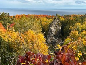 Sugar Loaf rock rises out of the middle of Mackinac Island amid a forest of fall color and blue water in the background