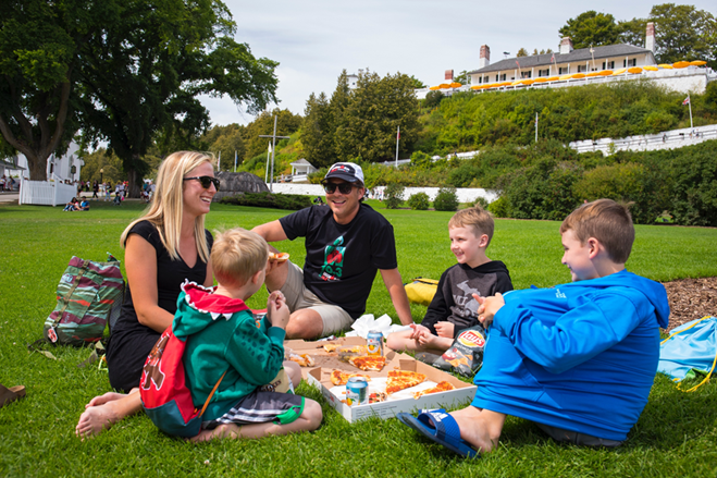 A family enjoys a pizza picnic in Mackinac Island’s Marquette Park at the foot of historic Fort Mackinac.