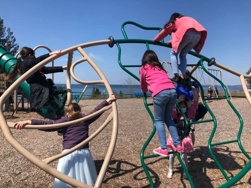Children play on the playground at Mackinac Island Public School with water in the background